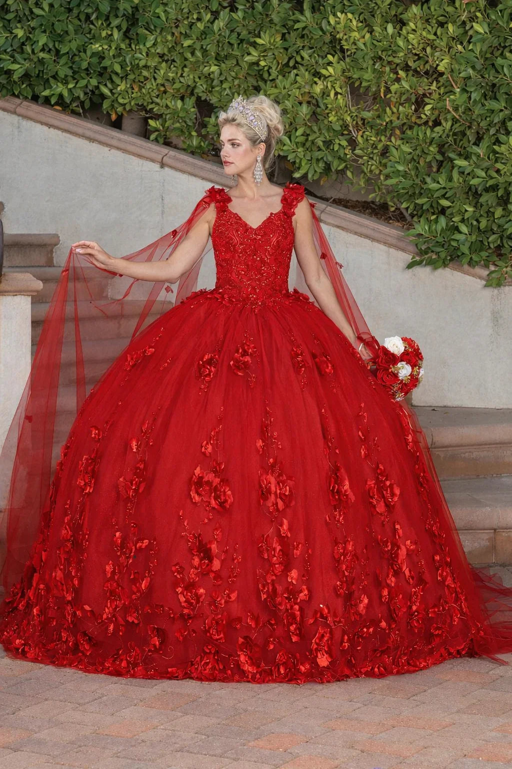 Mujer con vestido de XV años rojo con flores y corona, en jardín elegante.