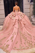 Vestido de quinceañera Ladivine rosa con bordados dorados, moño grande y cola larga.
