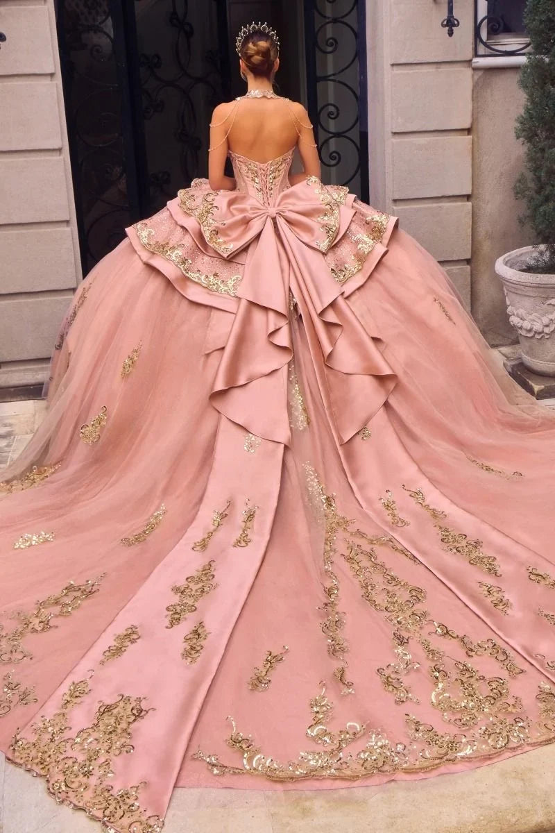 Vestido de quinceañera Ladivine rosa con bordados dorados, moño grande y cola larga.