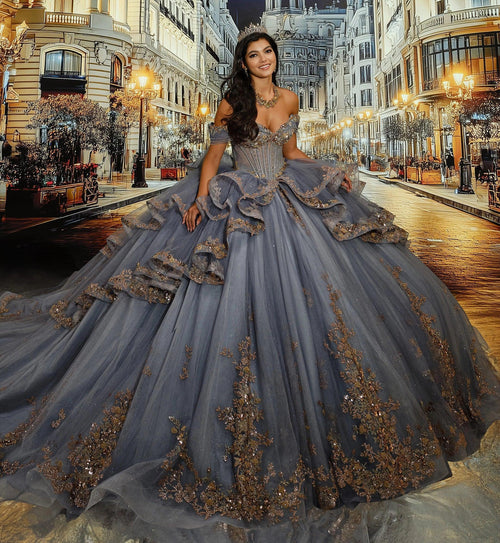 Joven con vestido de XV años azul grisáceo con encaje dorado y tiara en escenario urbano elegante.
