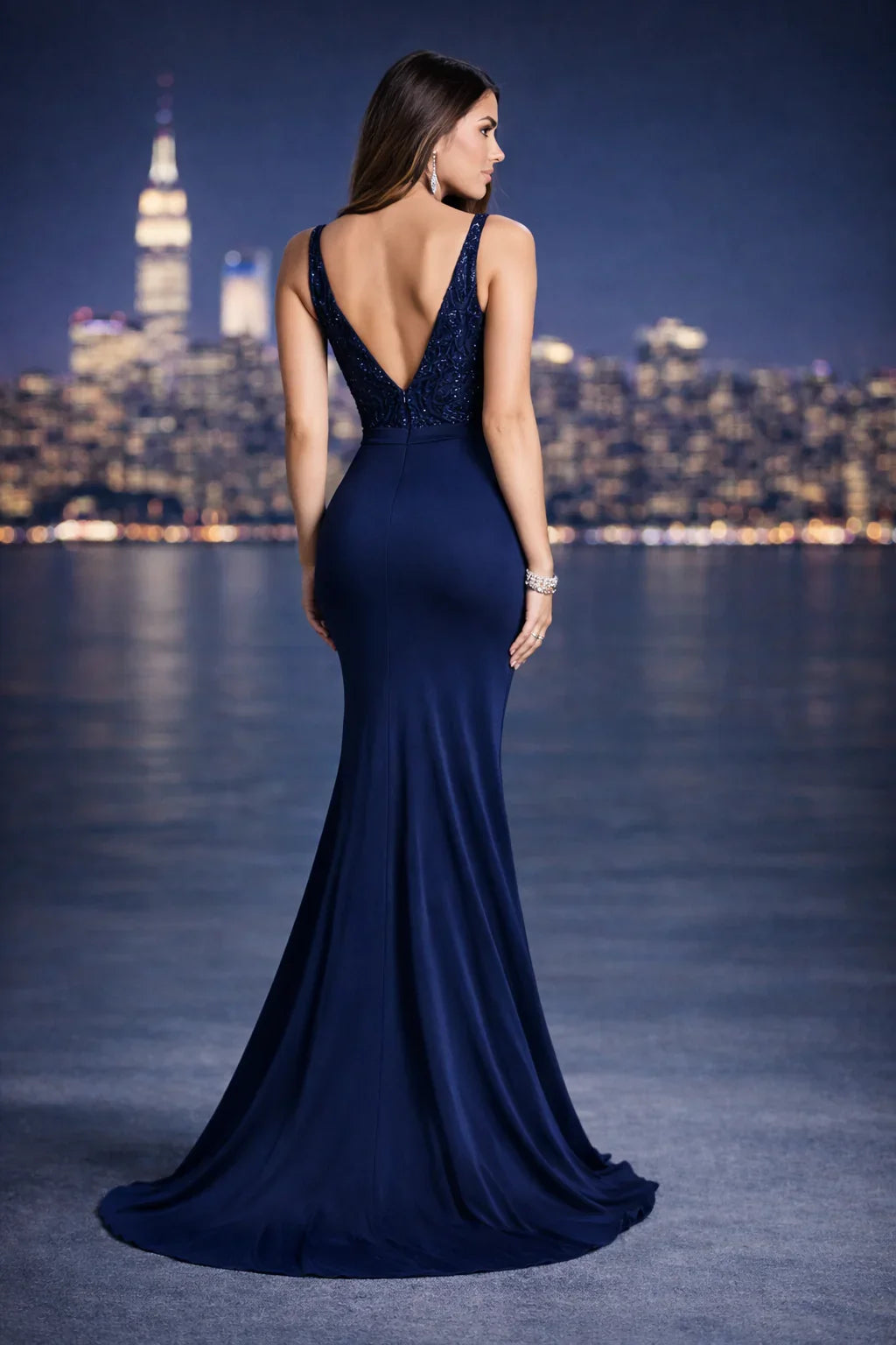 Mujer con vestido de fiesta azul marino entallado y escote en la espalda, fondo urbano nocturno.