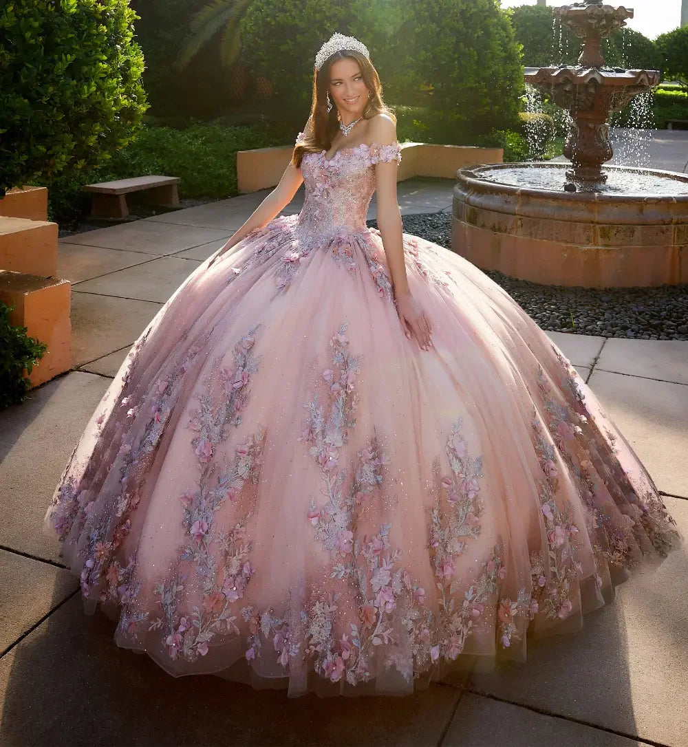 Joven con vestido de XV años rosa bordado con flores, tiara y fondo de jardín con fuente.