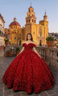 Joven con vestido de gala rojo brillante para XV años, posando frente a iglesia colonial al atardecer.