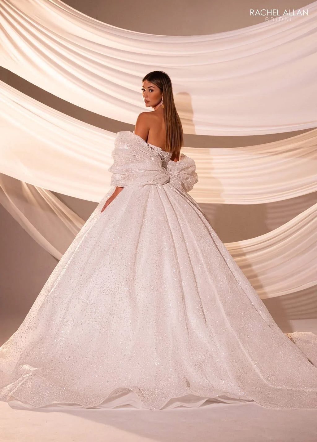 Mujer con vestido de novia elegante corte princesa, escote caído y lazo grande, fondo drapeado.