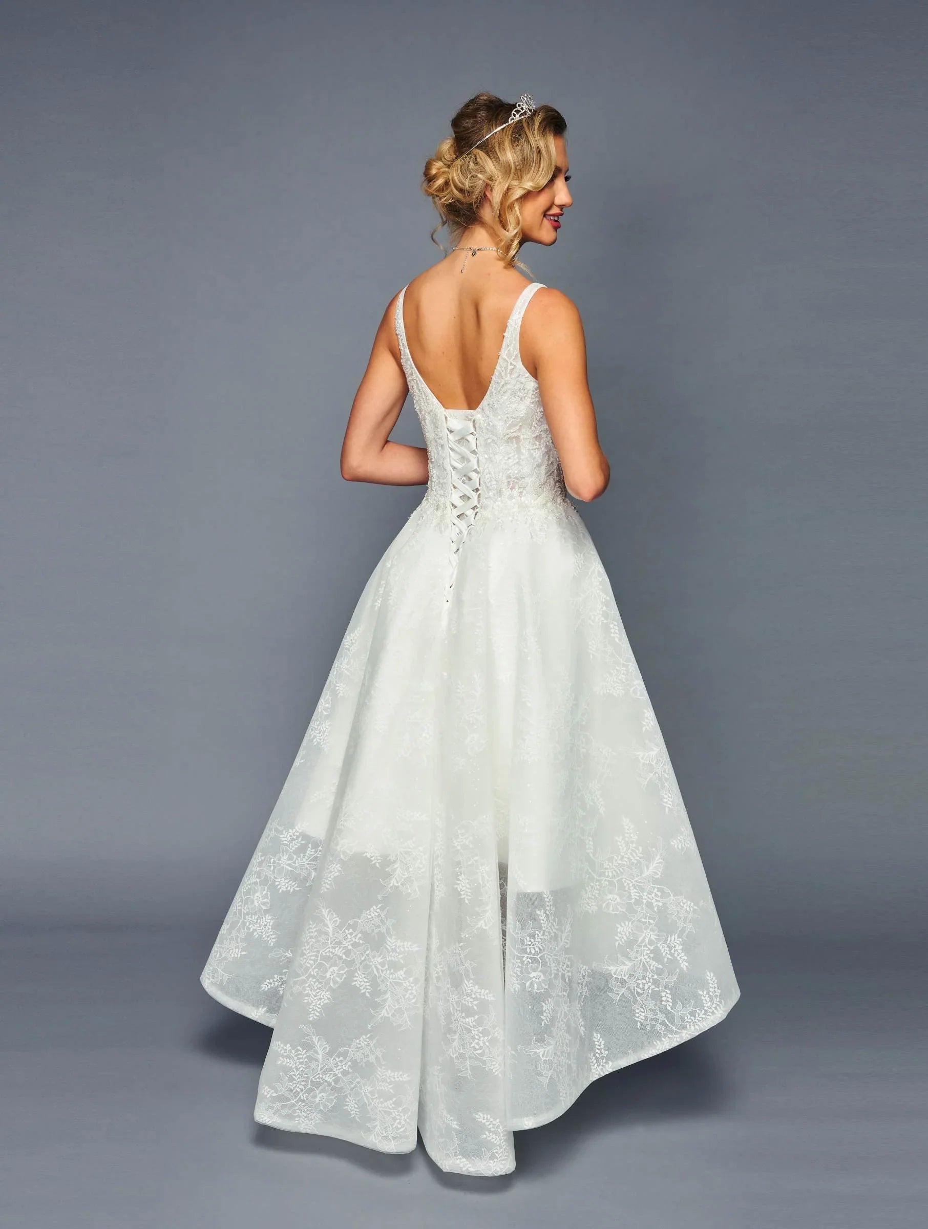 Mujer joven con vestido de novia blanco de encaje, escote en V y tiara, vista trasera elegante.