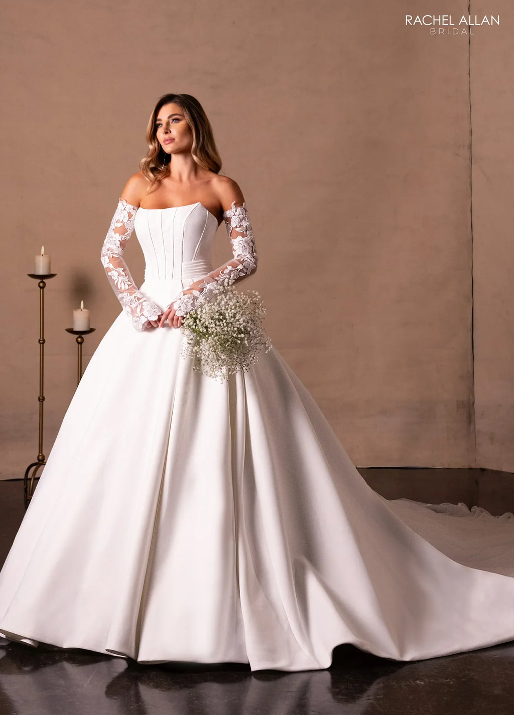 Mujer con vestido de novia blanco elegante, manga larga de encaje, ramo y fondo minimalista.