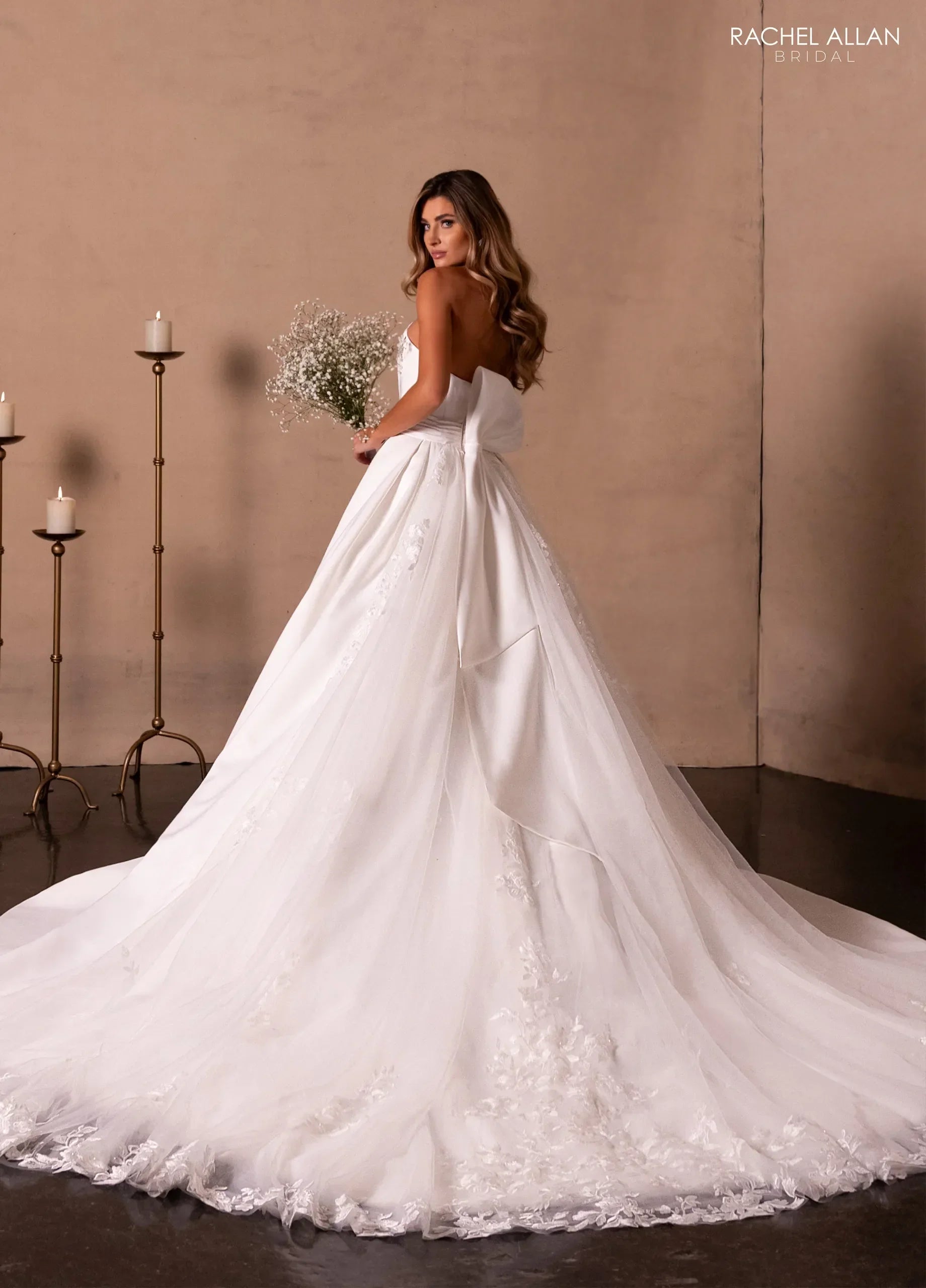 Mujer con vestido de novia blanco largo y cola, sosteniendo ramo, fondo elegante con velas.