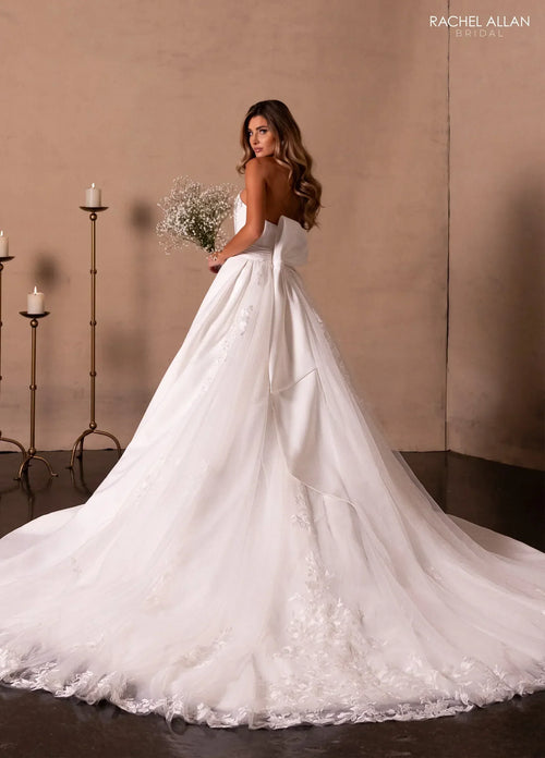 Mujer con vestido de novia blanco largo y cola, sosteniendo ramo, fondo elegante con velas.