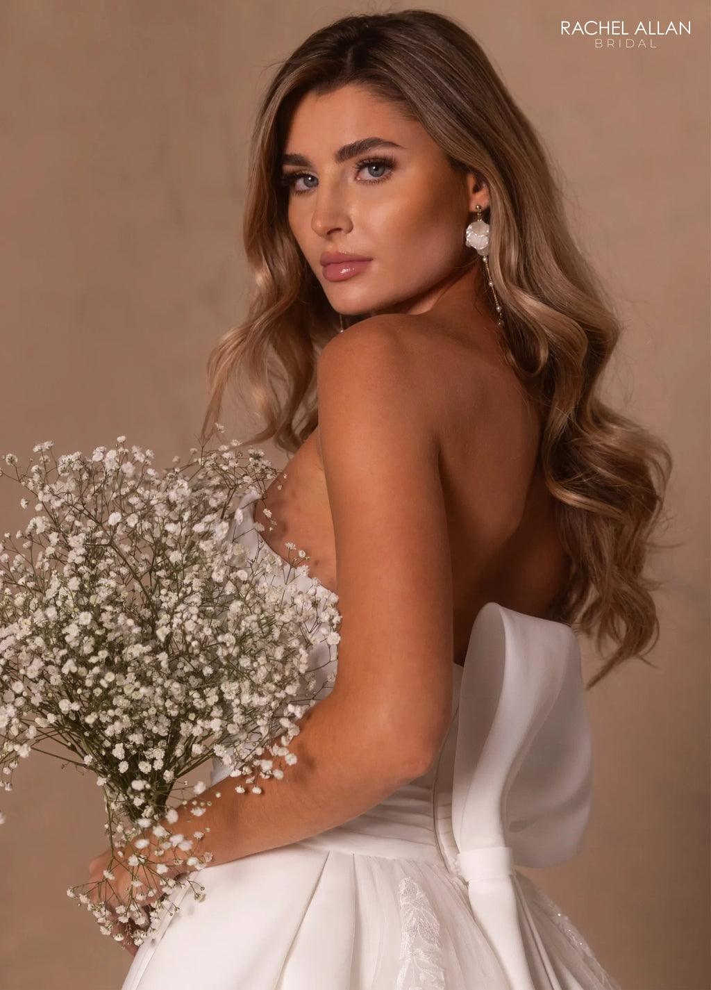 Mujer con vestido de novia blanco sin tirantes, ramo de flores blancas y peinado suelto ondulado.