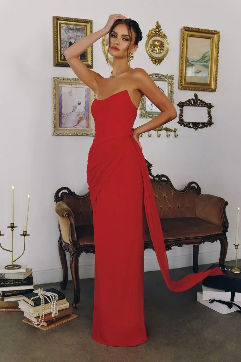 Mujer con vestido de fiesta largo rojo elegante, fondo vintage con sofá y cuadros, estilo formal.