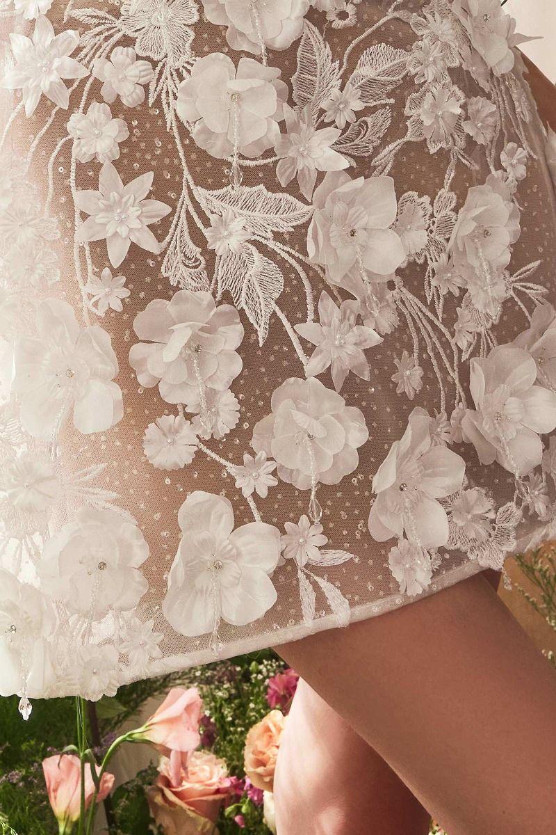 Detalle de vestido de fiesta corto con encaje floral blanco y aplicaciones en 3D
