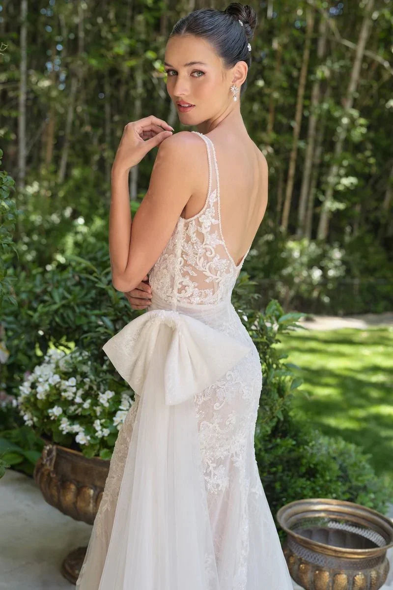 Mujer con vestido de novia de encaje blanco, escote en la espalda y moño grande, en jardín elegante