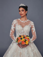 Novia con vestido DeKlaire Bridal corte línea A, encaje, manga larga y ramo de rosas naranjas.