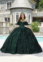 Joven con vestido de XV años verde esmeralda brillante y corona, posando frente a una mansión elegante.