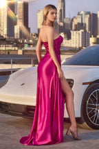 Mujer con vestido de fiesta largo magenta con abertura, fondo urbano y auto blanco.