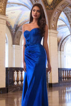 Mujer joven con vestido largo azul elegante, corsé y pedrería, en un salón lujoso.