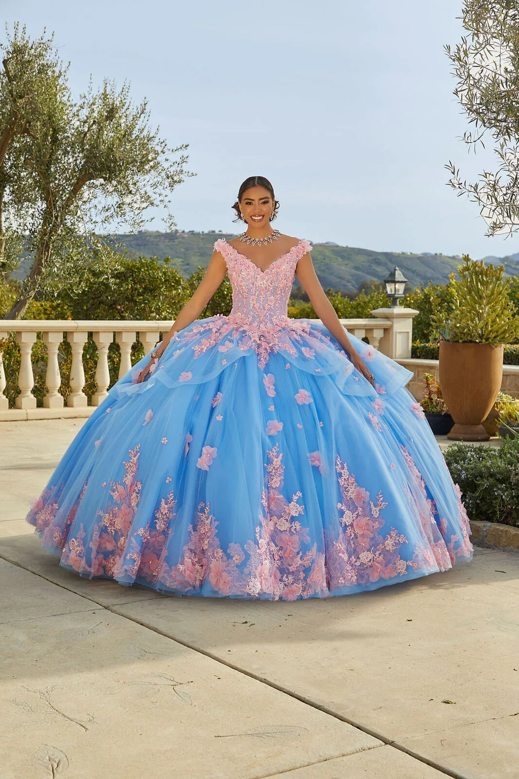 Joven con vestido de XV años azul y rosa, tul bordado floral, en jardín elegante