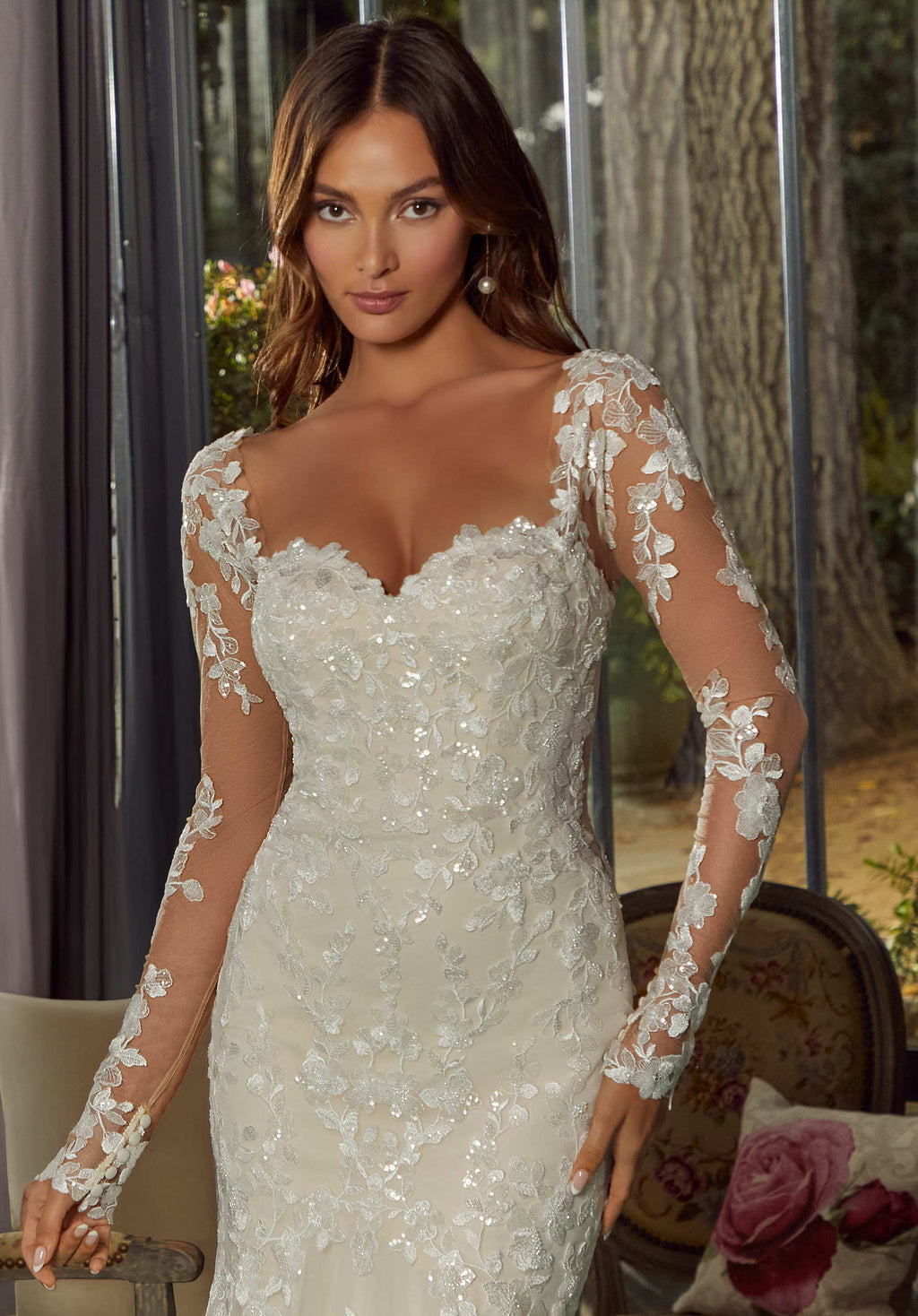 Novia con vestido blanco de encaje floral, lentejuelas y mangas largas transparentes.