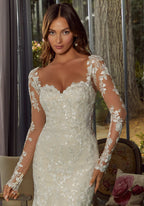 Novia con vestido blanco de encaje floral, lentejuelas y mangas largas transparentes.