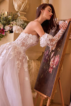 Novia con vestido blanco de encaje floral y mangas largas apoyada en un cuadro