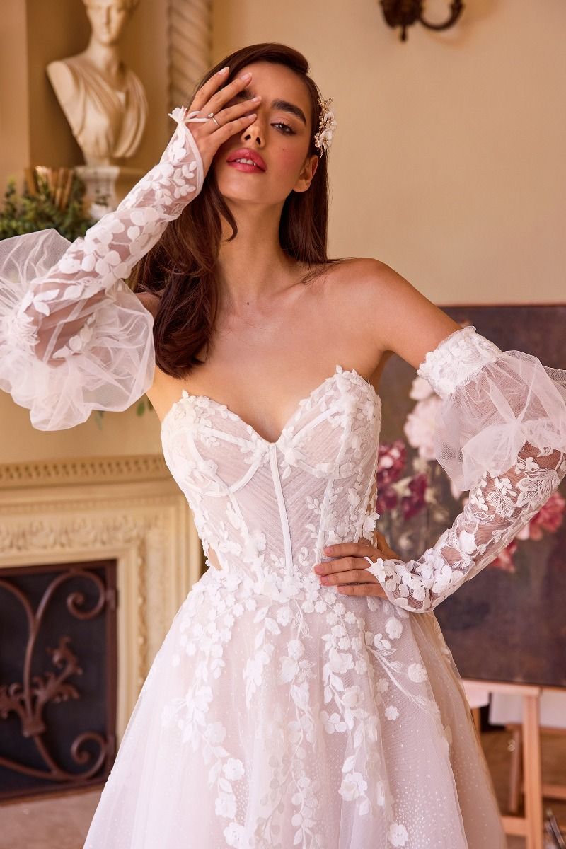 Novia con vestido blanco de encaje, corsé floral y mangas largas transparentes