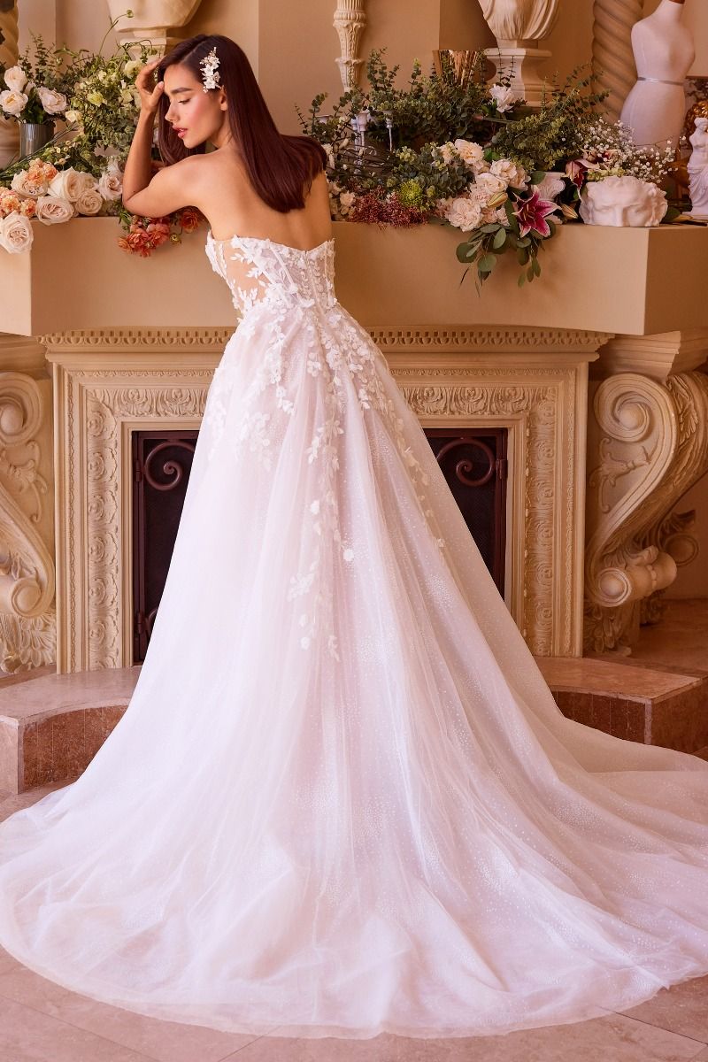 Novia de espaldas con vestido blanco bordado con encaje y falda brillante frente a chimenea.